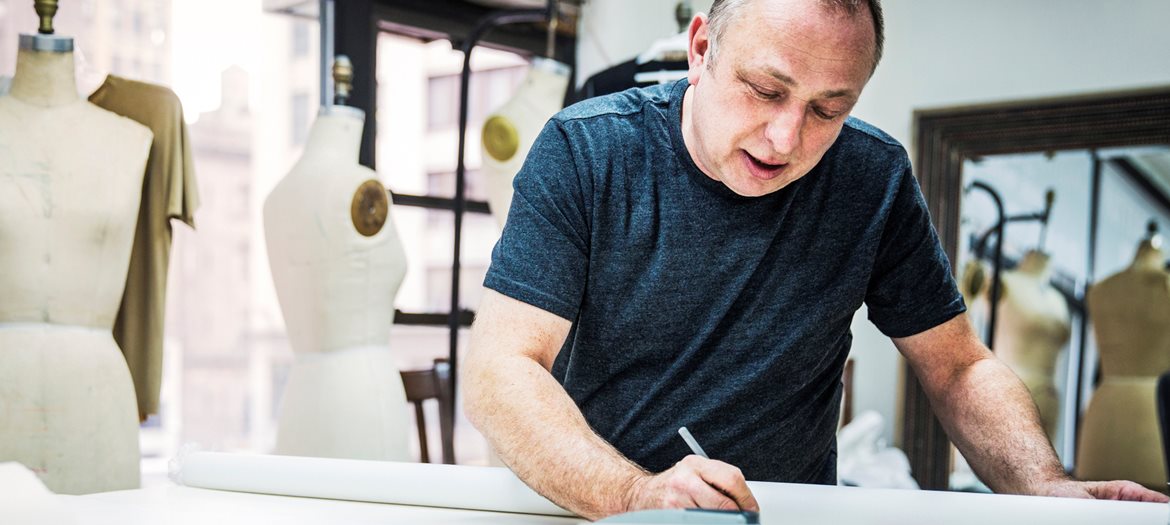 Man Marking Fabric in Sewing Studio with Dress Forms